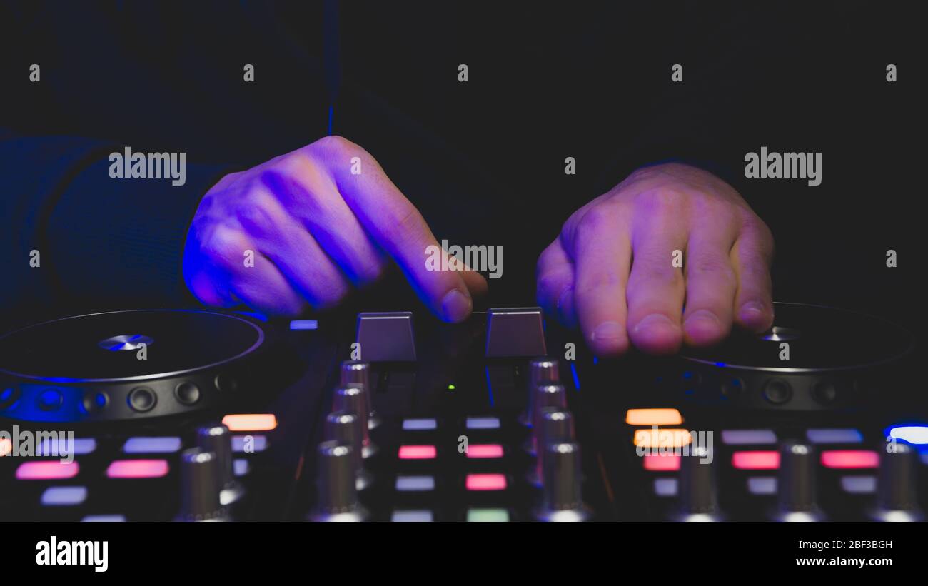 DJ plays music. sound mixer controller with knobs and sliders close up. hands on the mixing deck