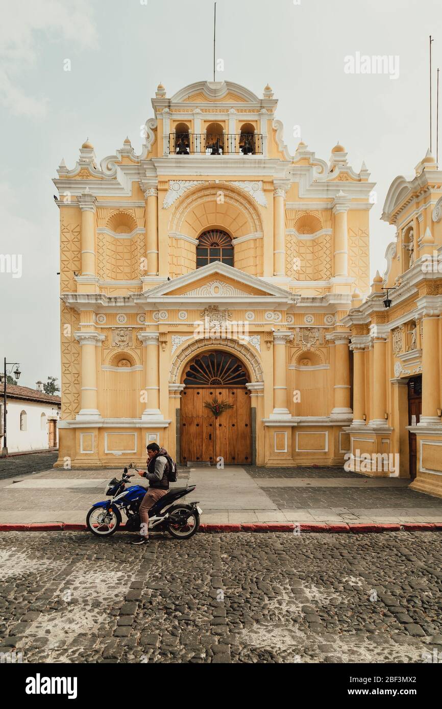 a man on his motorbike waiting in front of iconic Iglesia San Pedro church during coronavirus pandemic, unusually quiet Antigua Guatemala tourist town Stock Photo