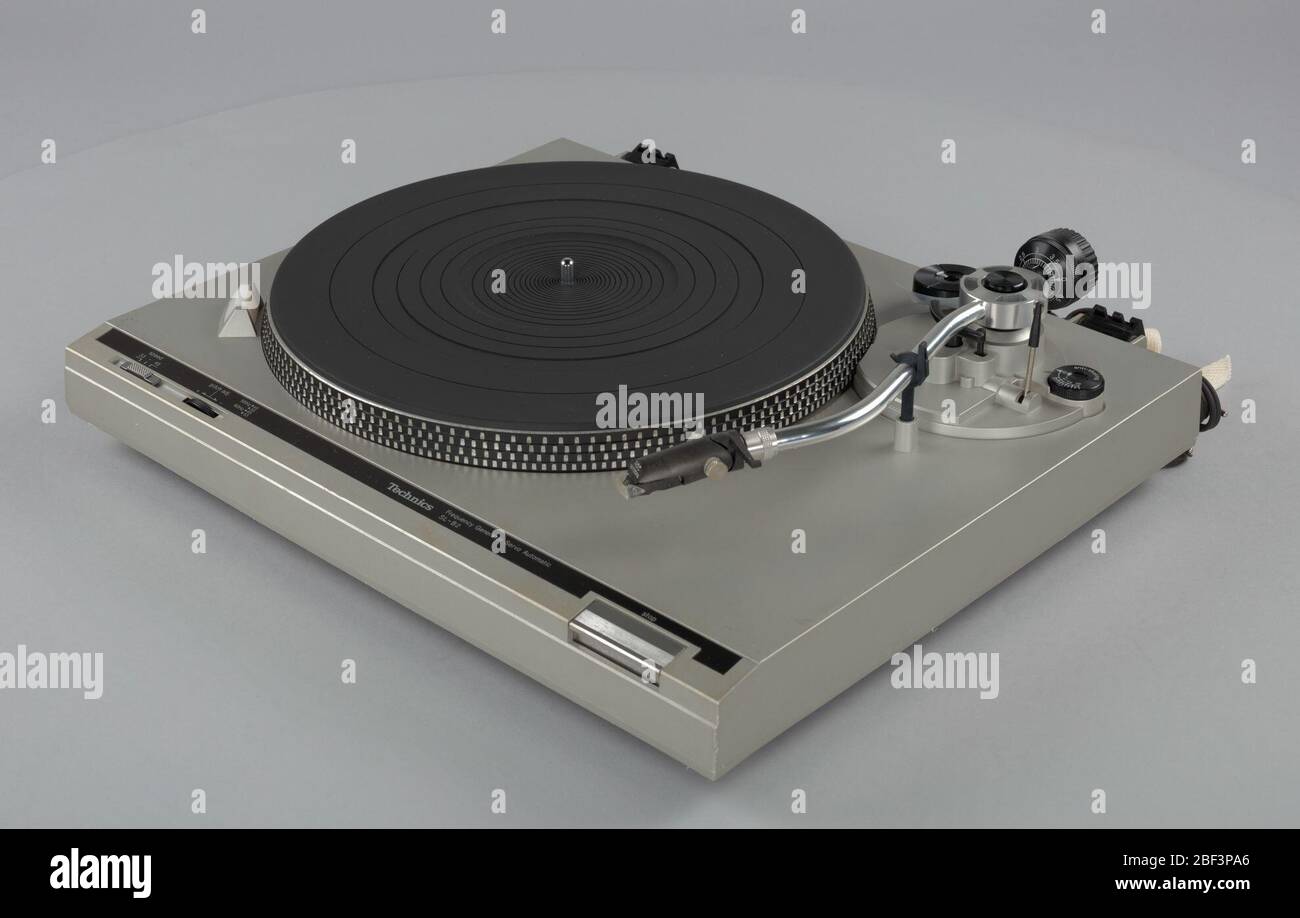 Turntable used as part of a DJ setup. A Technics SL-B2 turntable. The  turntable has a clear plastic covering and is mounted on a plastic plinth  or base, white in color. The