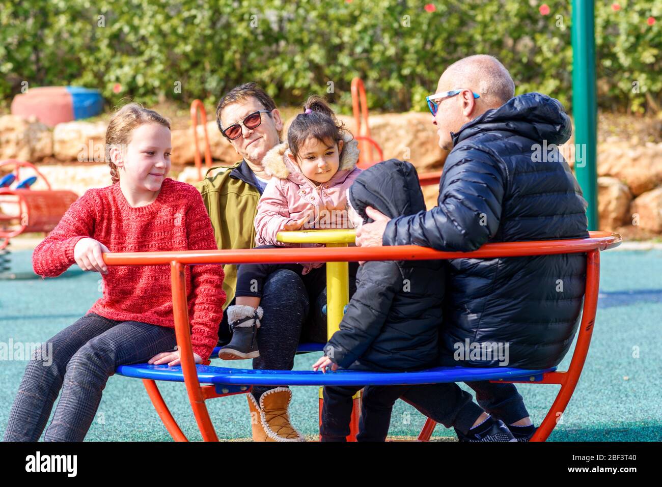 Pandemic end. Ending coronavirus quarantine, out of covid-19. Grandparents and grandchildren after long separation met. Happy family playing on rotating roundabout carousel at playground. Stock Photo