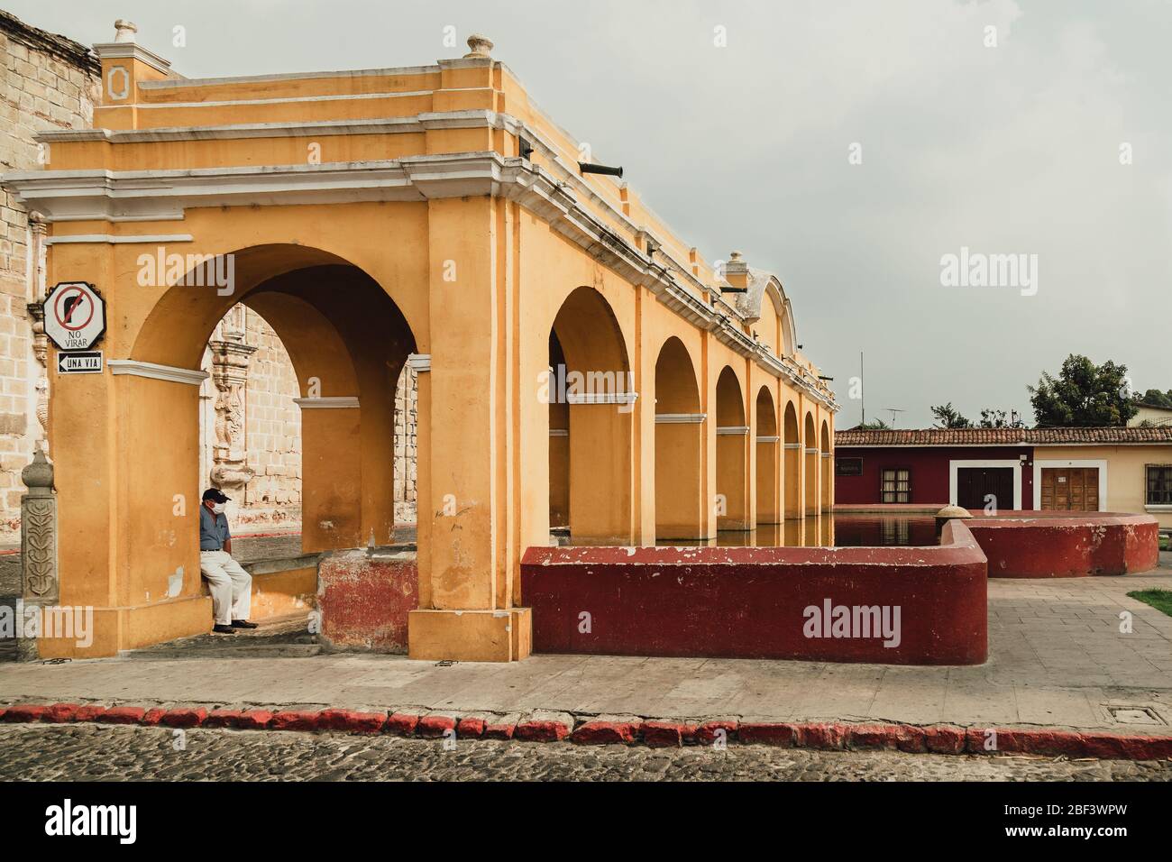 A man wearing face mask sitting under the arches of historic famous Tanque La Union in the colonial town Antigua Guatemala during coronavirus pandemic Stock Photo