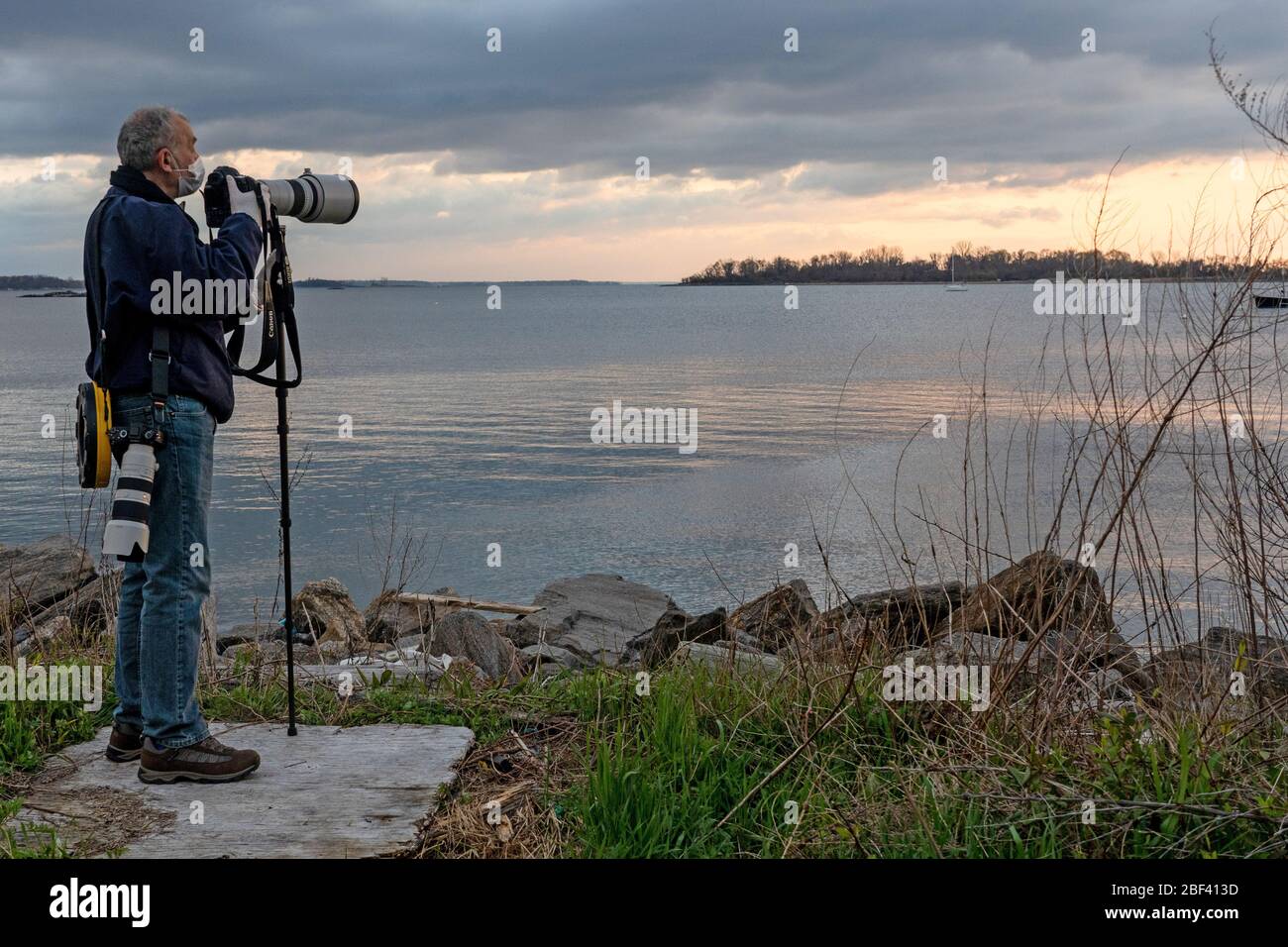 New York, United States. 16th Apr, 2020. News photographer Lev Radin, wearing gloves and a face mask takes pictures of ferry arriving at Hart Island, where unclaimed bodies of COVID-19 victims were buried on April 16, 2020 in Bronx. Credit: SOPA Images Limited/Alamy Live News Stock Photo