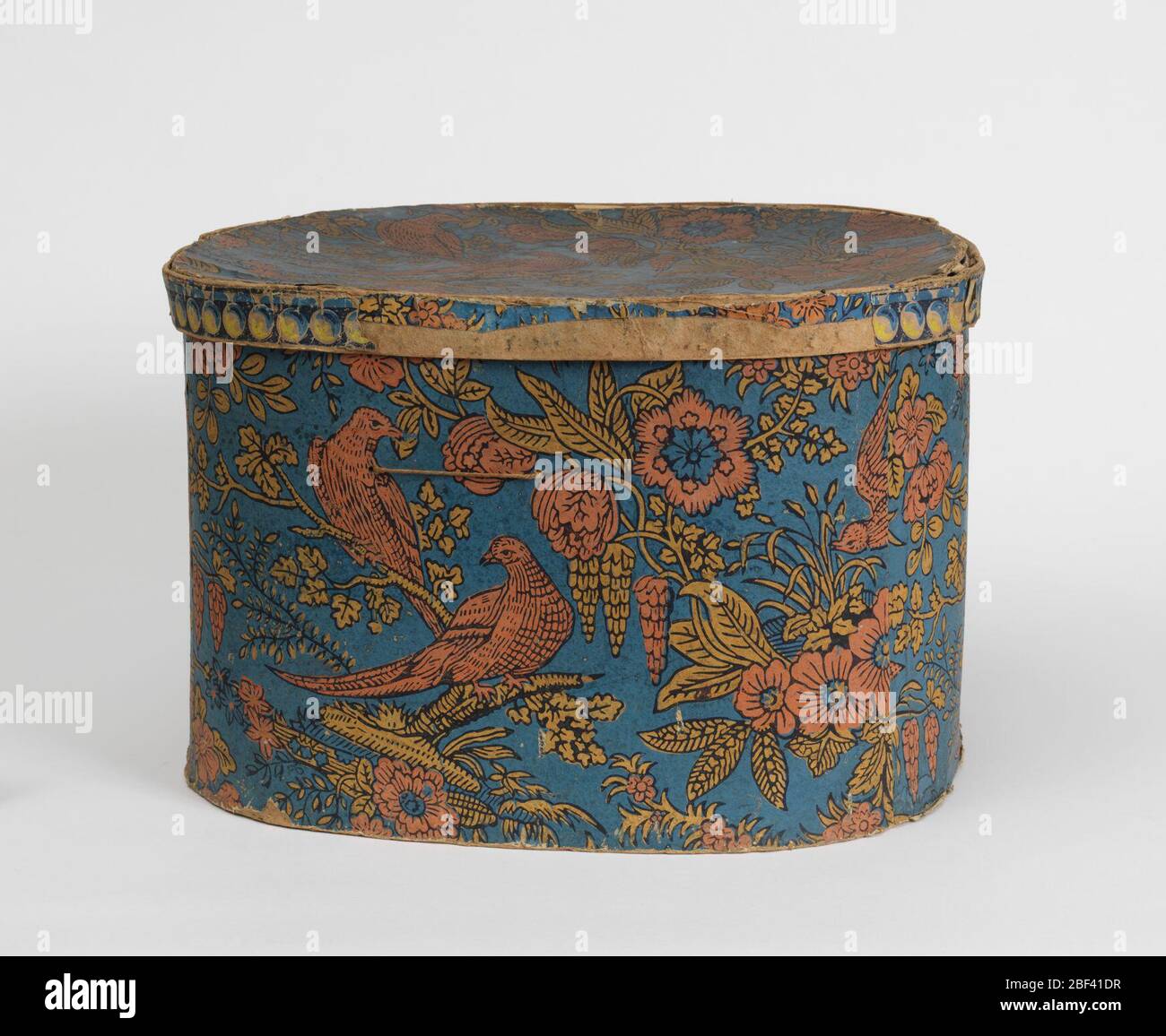 Bandbox. Block print repeat design wallpaper pattern: on blue background, two salmon-colored birds on yellow limb with leaves, sprays of salmon and yellow flowers and leaves, salmon-colored bird in flight. Over-all diagonal movement of pattern. Stock Photo