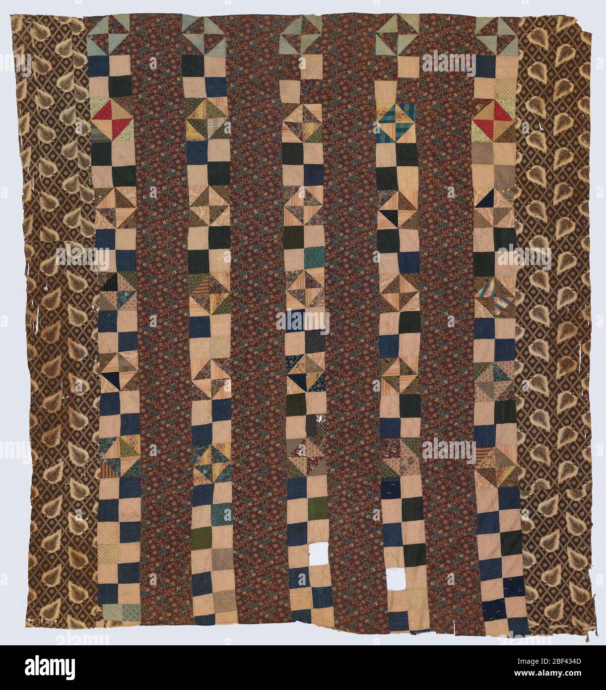Chintz Bar and Broken Dishes. Patchwork quilt top made of six broad whole-cloth strips and five narrow patchwork strips. The patchwork strips are made up of small square and triangular pieces in tans, browns, and dark blue. Stock Photo