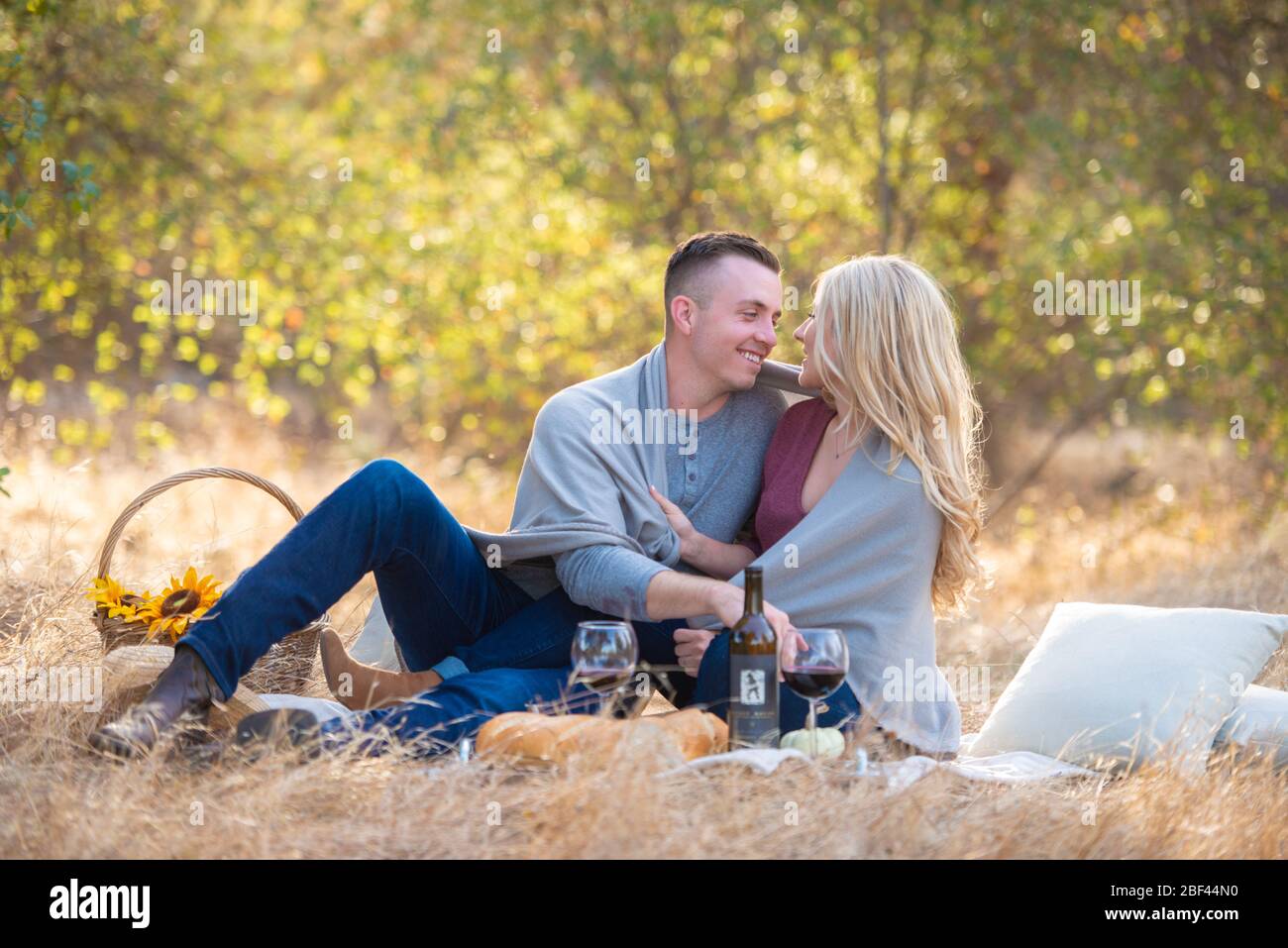 A couple having a picnic and drinking wine outdoor in the tall grass ...
