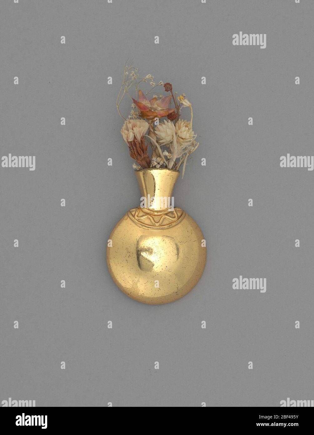 Bouquet holder vase shape pin. Small brass bouquet holder pin. The vase is urn shaped with curvilinear decoration around neck. The back is flat with pin for attachment a garment.Flowers used for personal adornment were a popular fashion accessory throughout the 1800s up to the mid-1900s. Stock Photo