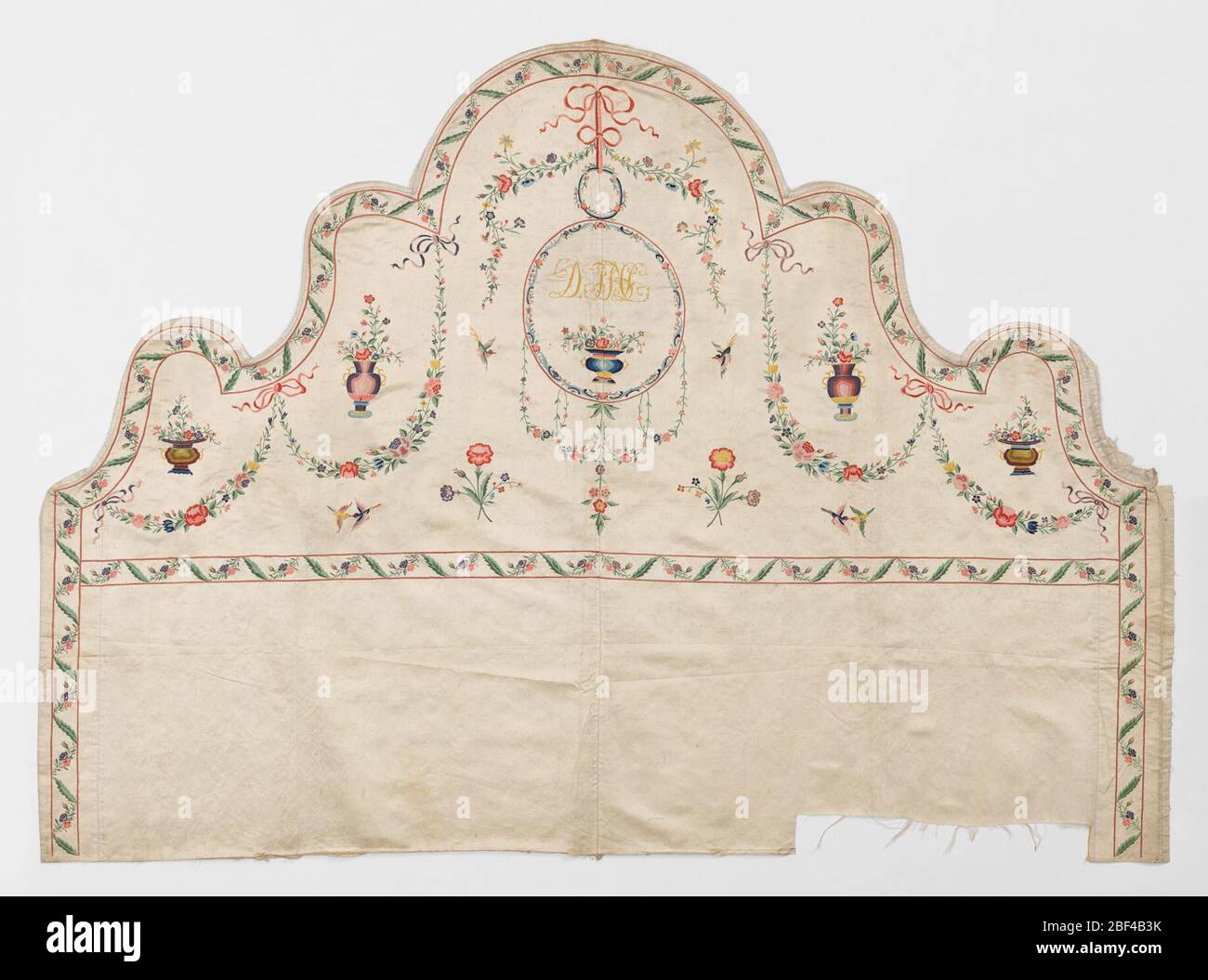 Headboard panel. Embroidered headboard panel of ivory satin worked in multicolored silks in a pattern of delicate floral garlands, jars of flowers, ribbons and birds. Initials (illegible) embroidered in a central medallion. Stock Photo