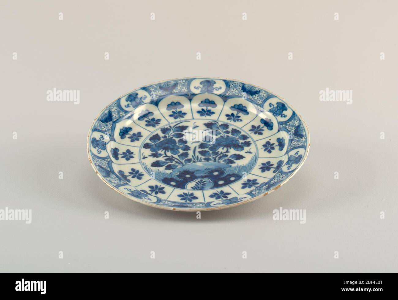 Plate. Circular plate painted in underglaze blue on white; center with chinoiserie scene of flowers, rocks, insects; on cavetto with 14 uniform panels with flowers; around rim with evenly-spaced reserves of floral motifs on diaper pattern; bottom, low foot rim, 7 gro Stock Photo