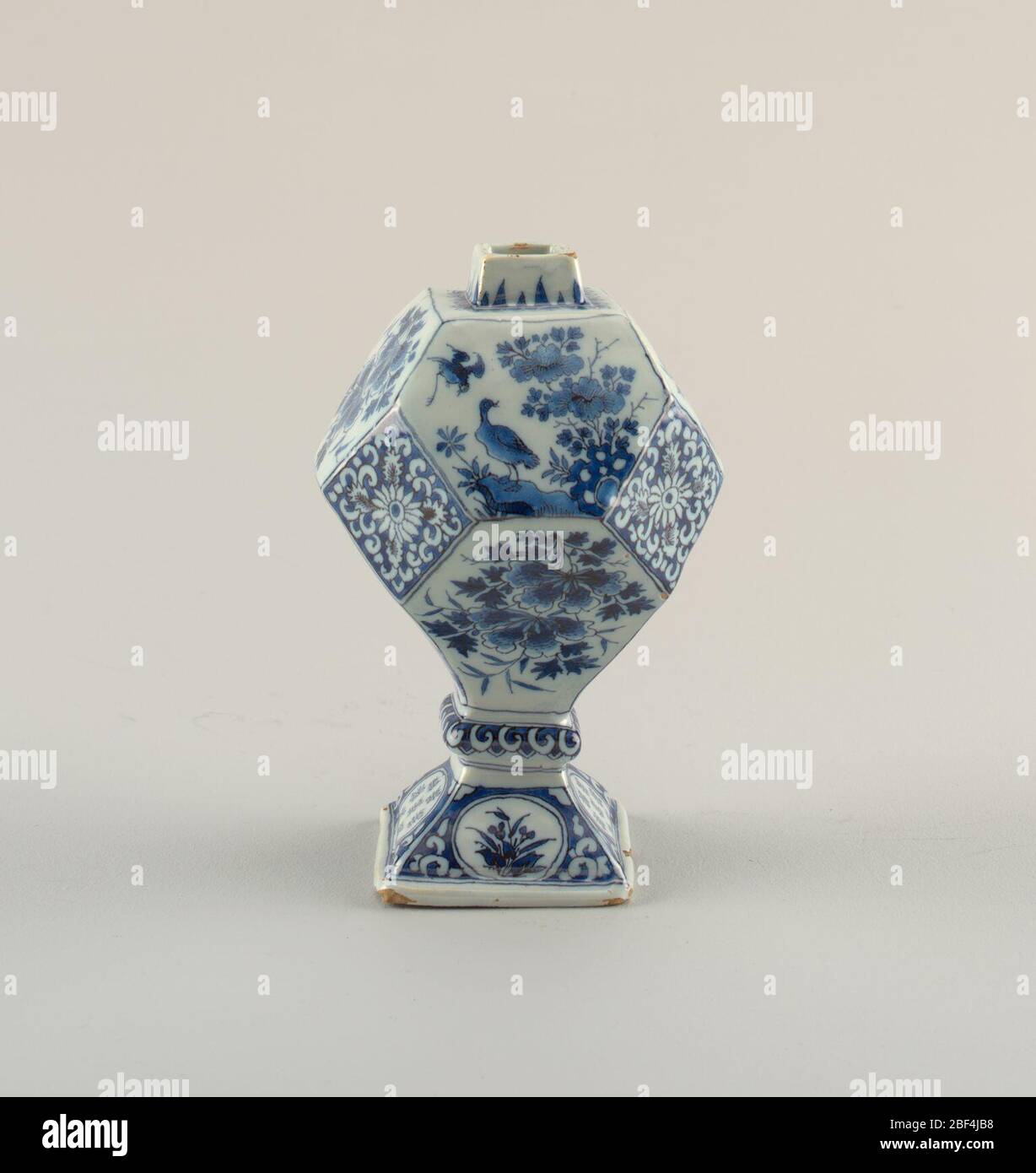 Bottle. Twelve-faceted body with short square-sided neck on a 4-sided domed foot with knop; painted in underglaze blue on white with chinoiserie designs of flowers and birds, leaves, pseudo-Chinese characters in reserve on base. Stock Photo