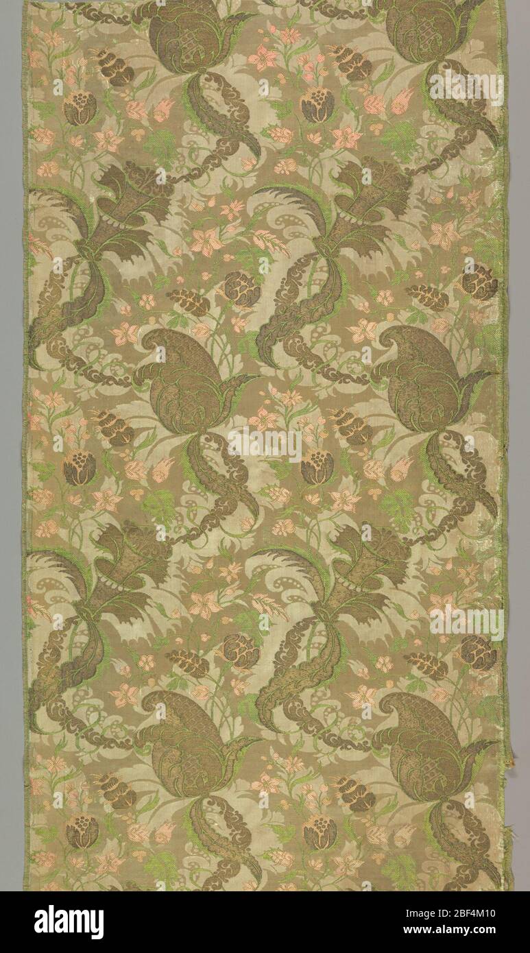 Textile. Tan colored silk damask brocaded in green and pink silk with metallic yarns. Brocading bound in twill by warps. Design in the ‘bizarre’ style shows a pattern of large florals with serpentine chains composed of scrolls. Both selvages persent. Stock Photo