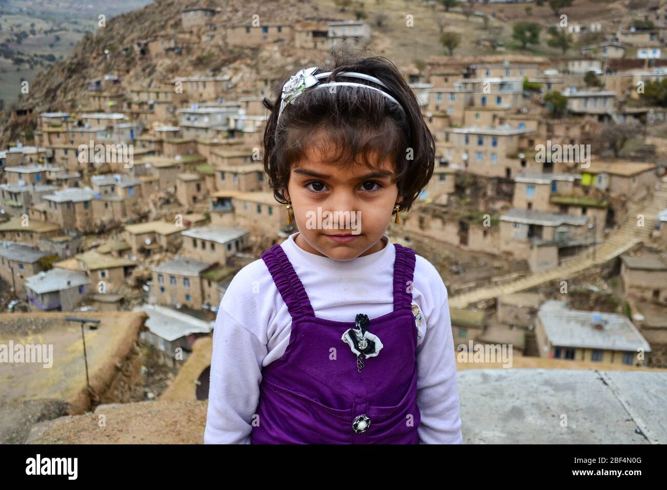 Palangan, Iranian Kurdistan - November 15, 2013: Portrait of cute and little Kurdish girl posing with Palangan stone village in the background Stock Photo