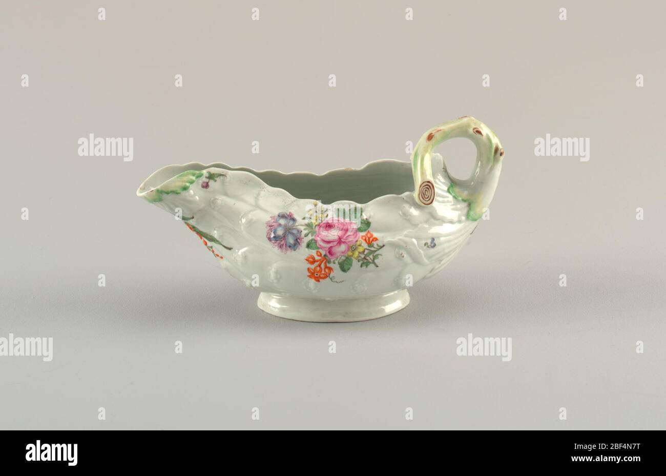 LeafShaped Sauceboat. White porcelain leaf-shaped sauce boat with a branch handle. Decorated with small flower details. Stock Photo