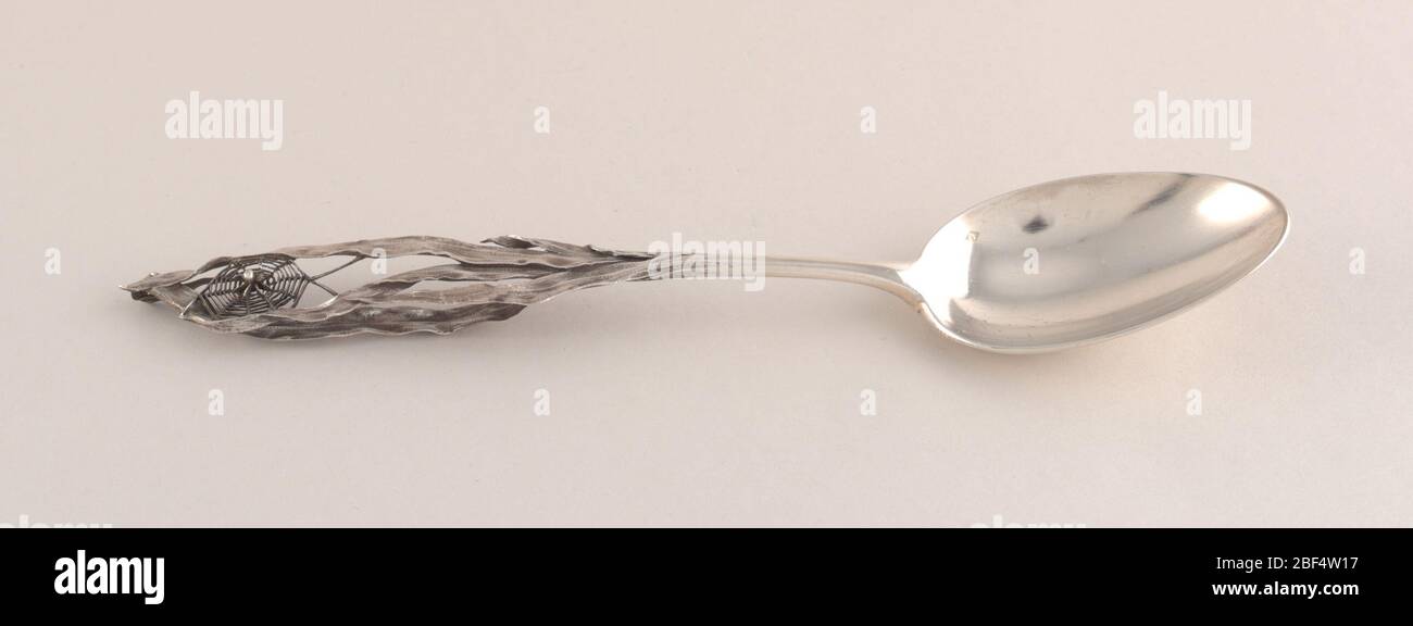 Dessert spoon. Handle in the form of a patinated spider on spider's web suspended between blades of grass. Stock Photo