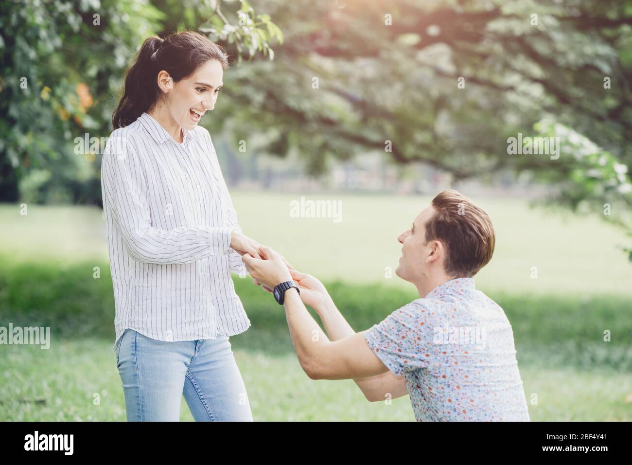 Photos of engagements, marriage proposals, and newly engaged couples lover young man and lady outdoor green park. Stock Photo
