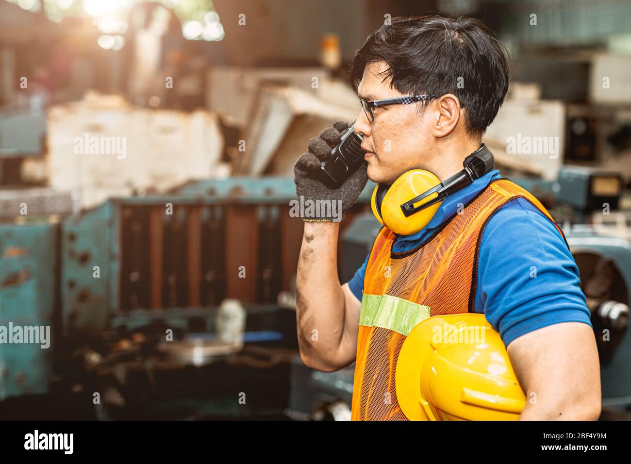Asian engineer worker with protection suit set hard working in factory handle communication radio looking camera and smile. Stock Photo