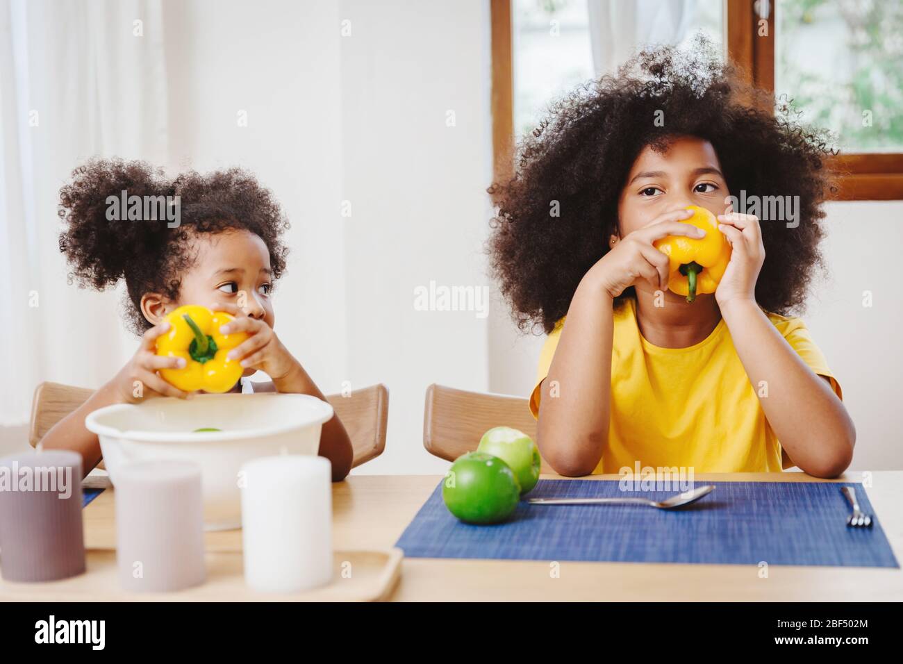 Little cute younger sister looking wondering and imitated her older sister try to eating bell pepper Stock Photo