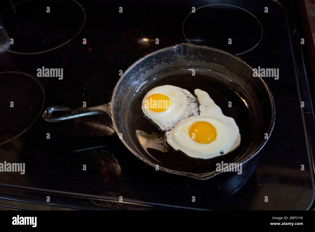 Breakfast Two sunny side up eggs fsliding out of a cast iron skillet on white plate Stock Photo