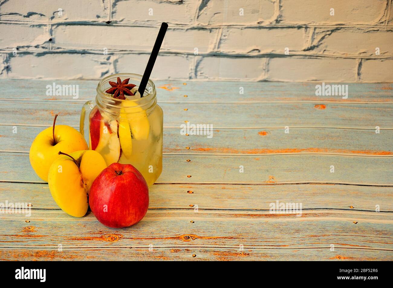 Glass mug of juice with ice, anise and ripe apples nearby on a wooden table. Close-up. Stock Photo