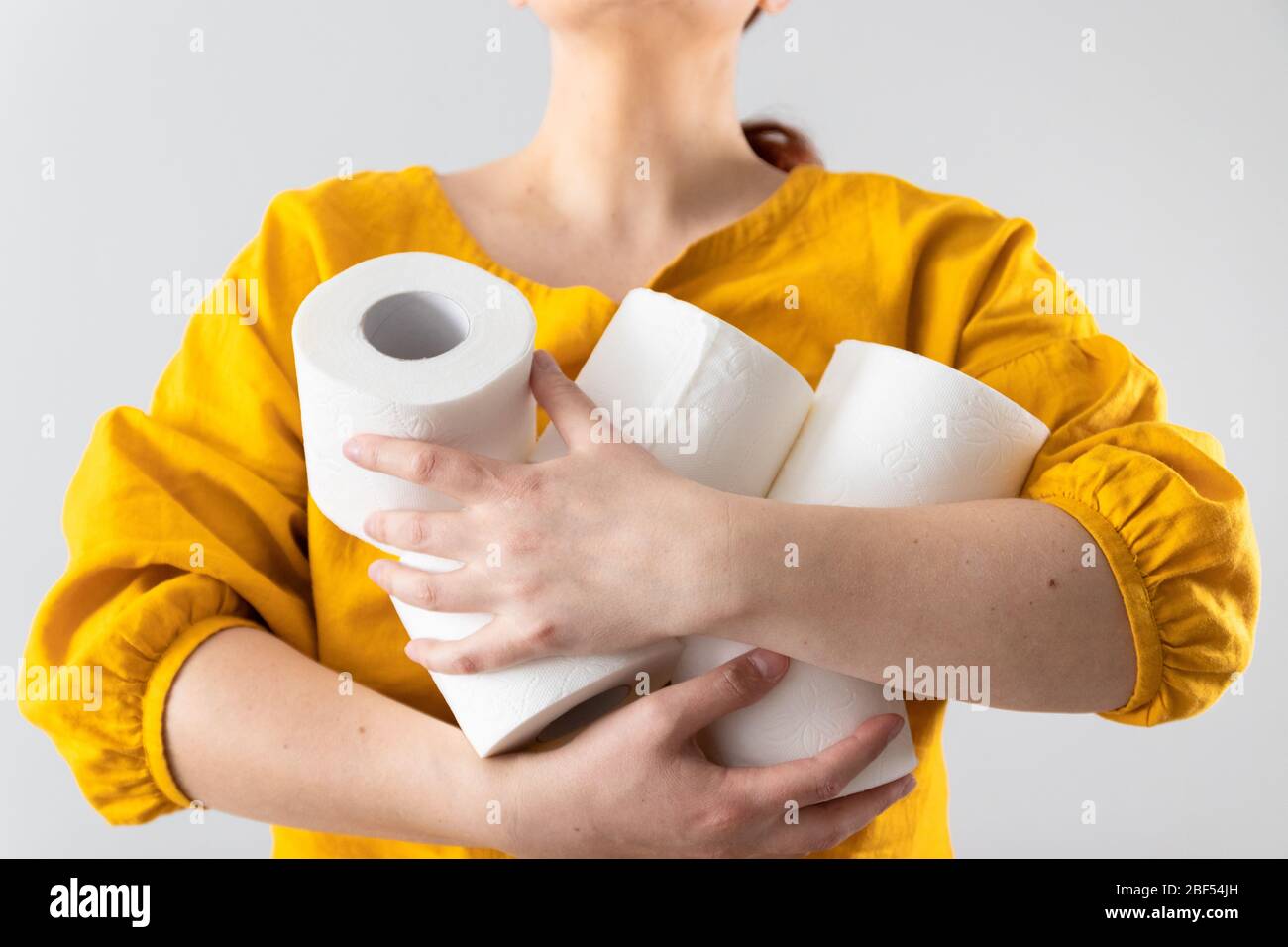 Female hands holds many rolls of toilet paper on a gray wall background