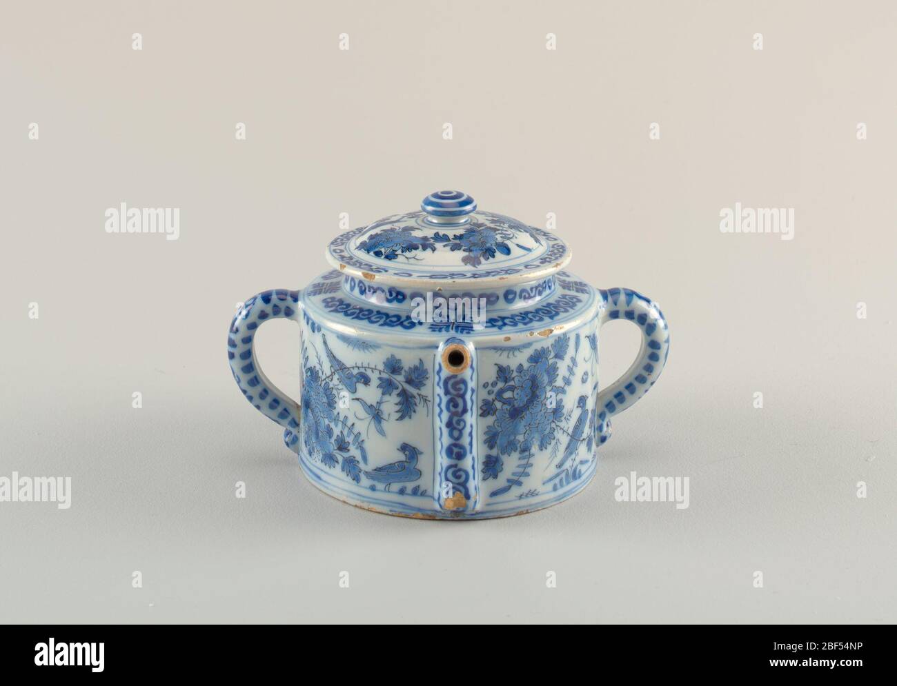 Posset Pot. Cylindrical body with straight sides; 2 loop handles opposite sides; spout rises along side body, projects horizontally from squared shoulder; domed lid with wide lip and flattened knop finial; painted in underglaze blue on white with chinoiserie birds, flower Stock Photo