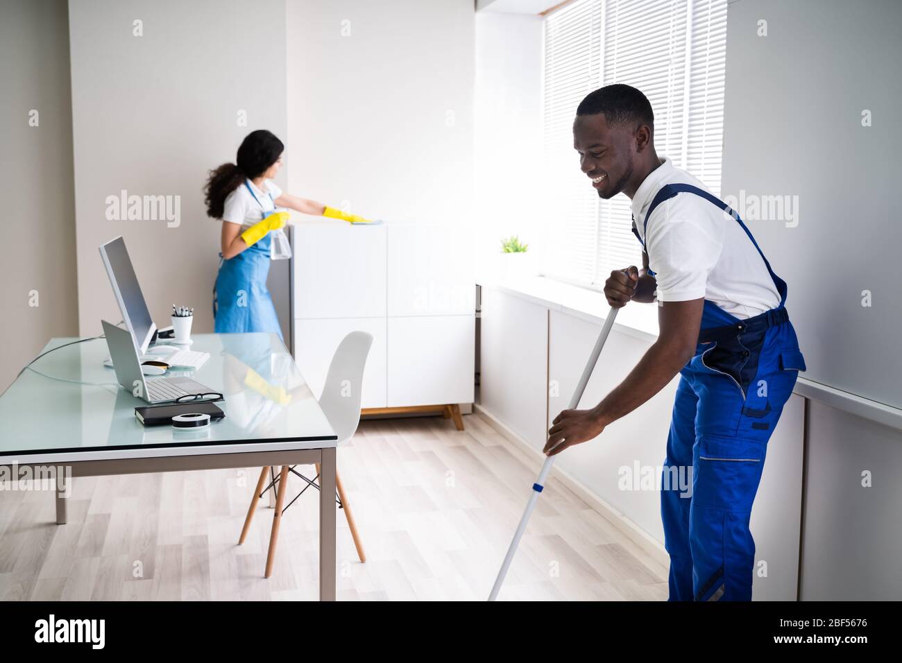 Young Male And Female Cleaners Cleaning Office Stock Photo