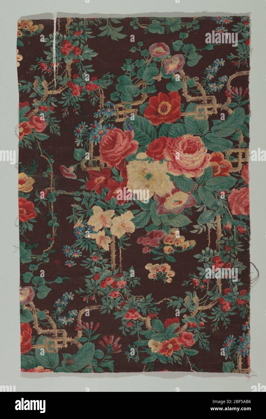 Textile. Large bouquet of roses with smaller climbing rose brances and other flowers. Background of dark brown and floral pattern in shades of red, green, blue and white. Stock Photo