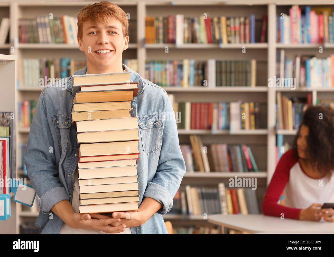 Portrait of male student with big stack of books in library Stock Photo ...