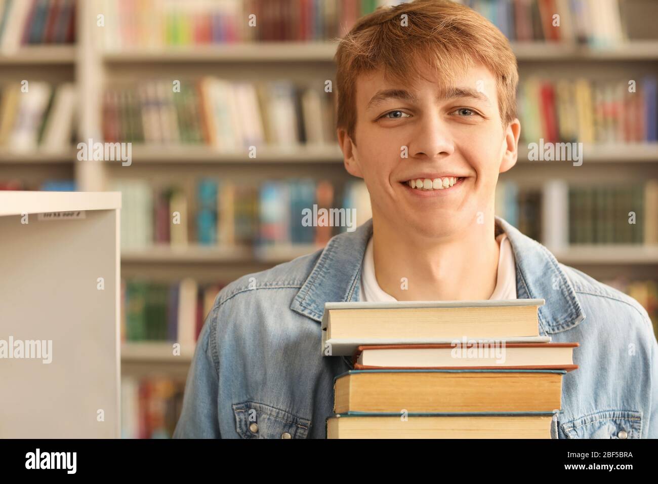 Portrait of male student with big stack of books in library Stock Photo ...