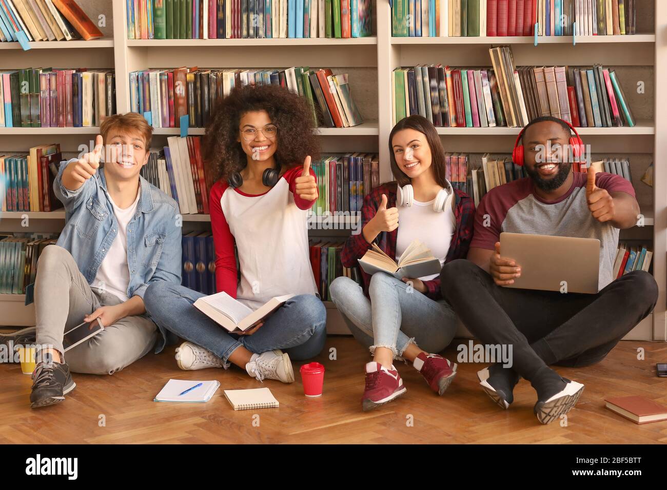 Young students showing thumb-up gesture in library Stock Photo - Alamy