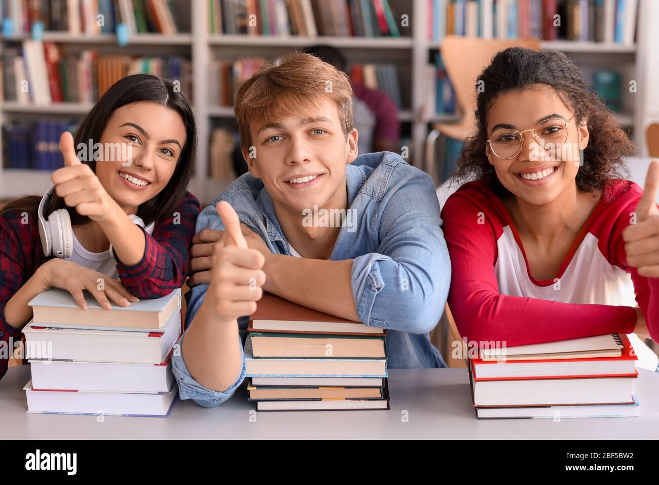 Young students showing thumb-up gesture in library Stock Photo - Alamy