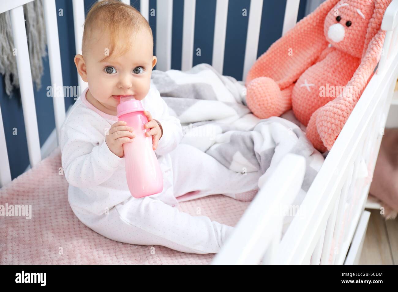 Cute baby drinking milk from bottle in crib Stock Photo Alamy
