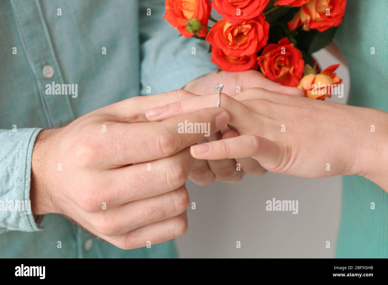 Young man putting ring on finger of his fiancee after marriage proposal, closeup Stock Photo