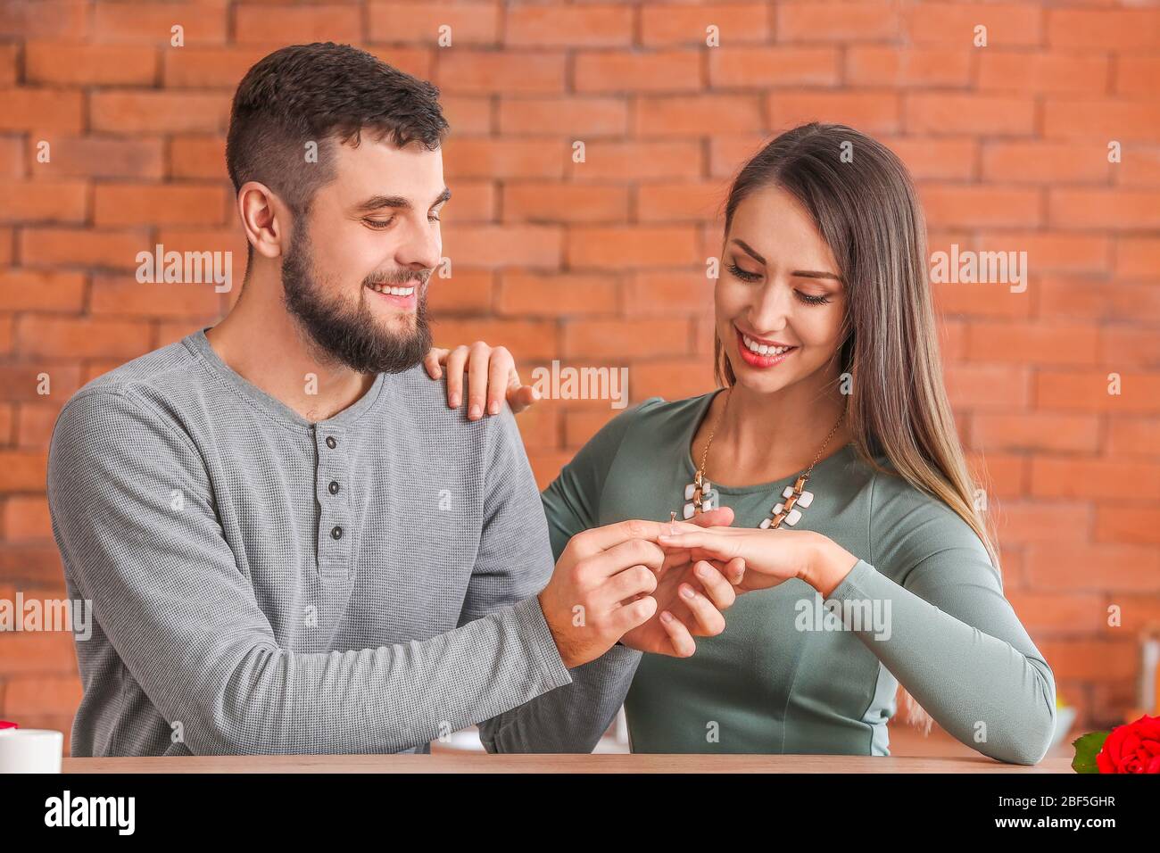 Young man putting ring on finger of his fiancee after marriage proposal at home Stock Photo