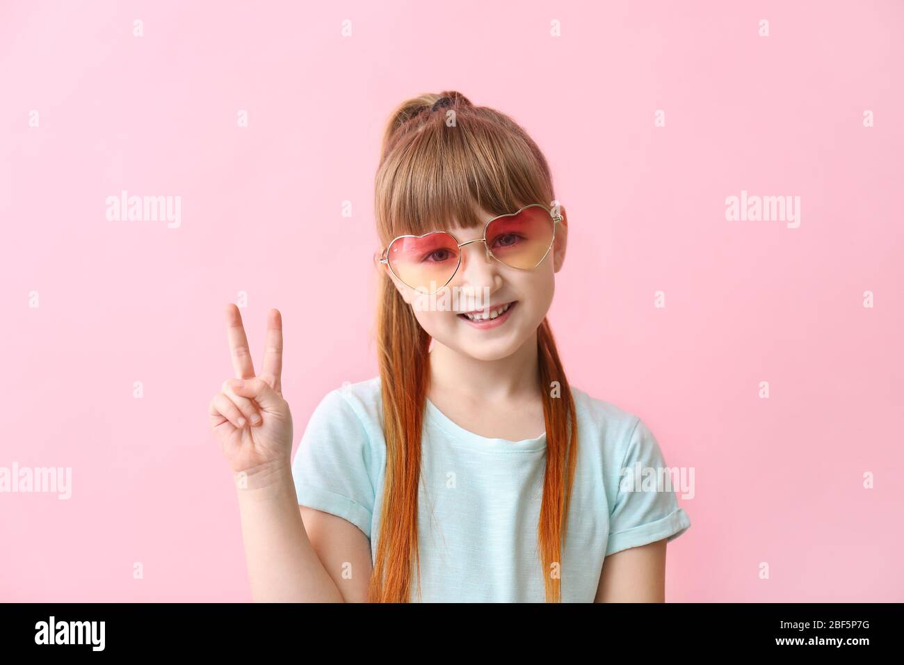 Funny little girl with sunglasses showing victory gesture on color
