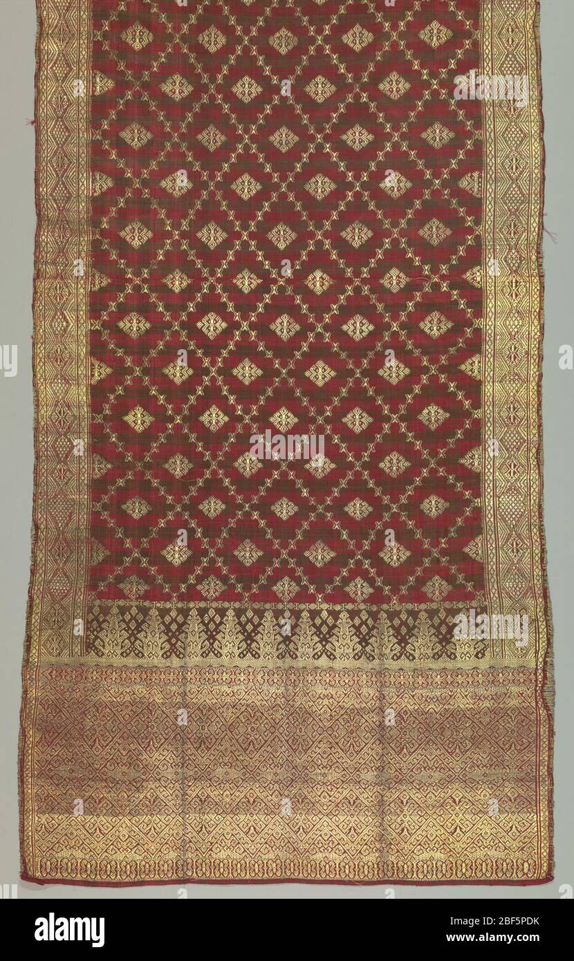 Textile. Long silk textile, probably a shoulder cloth (selendang), in dark brown against red. Plaid ground with all-over brocading of geometric pattern with center motif on main ground. Heavy brocading in borders. Stock Photo