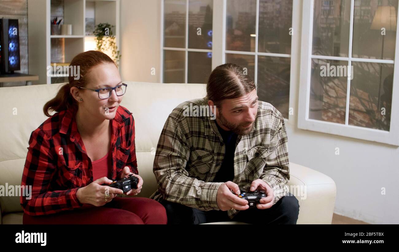 Hipster couple sitting on sofa playing video games using wireless controller. Man and woman giving high five. Stock Photo