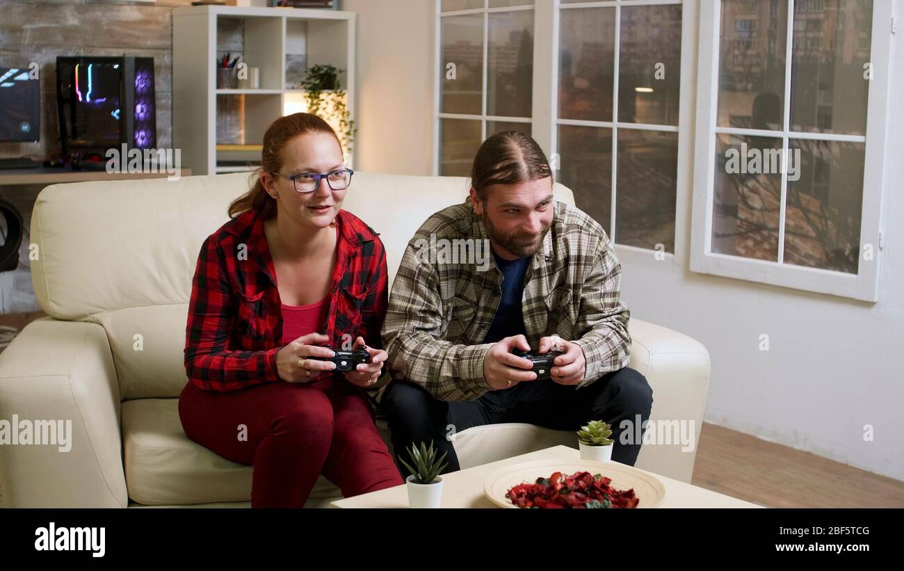 Couple in their 30's relaxing playing video games using wireless controllers. Happy relationship. Stock Photo