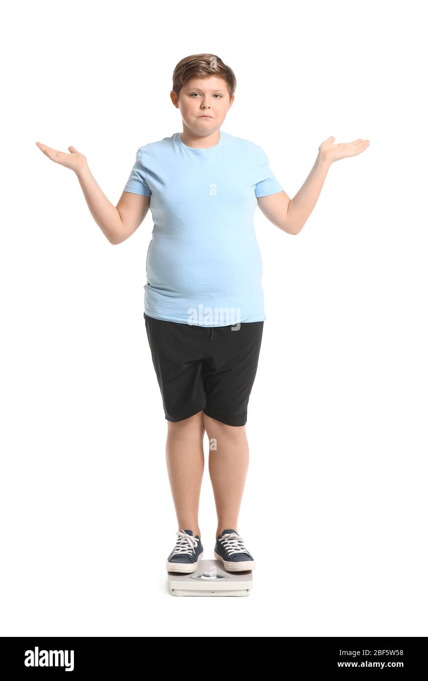Overweight boy standing on scales against white background Stock Photo