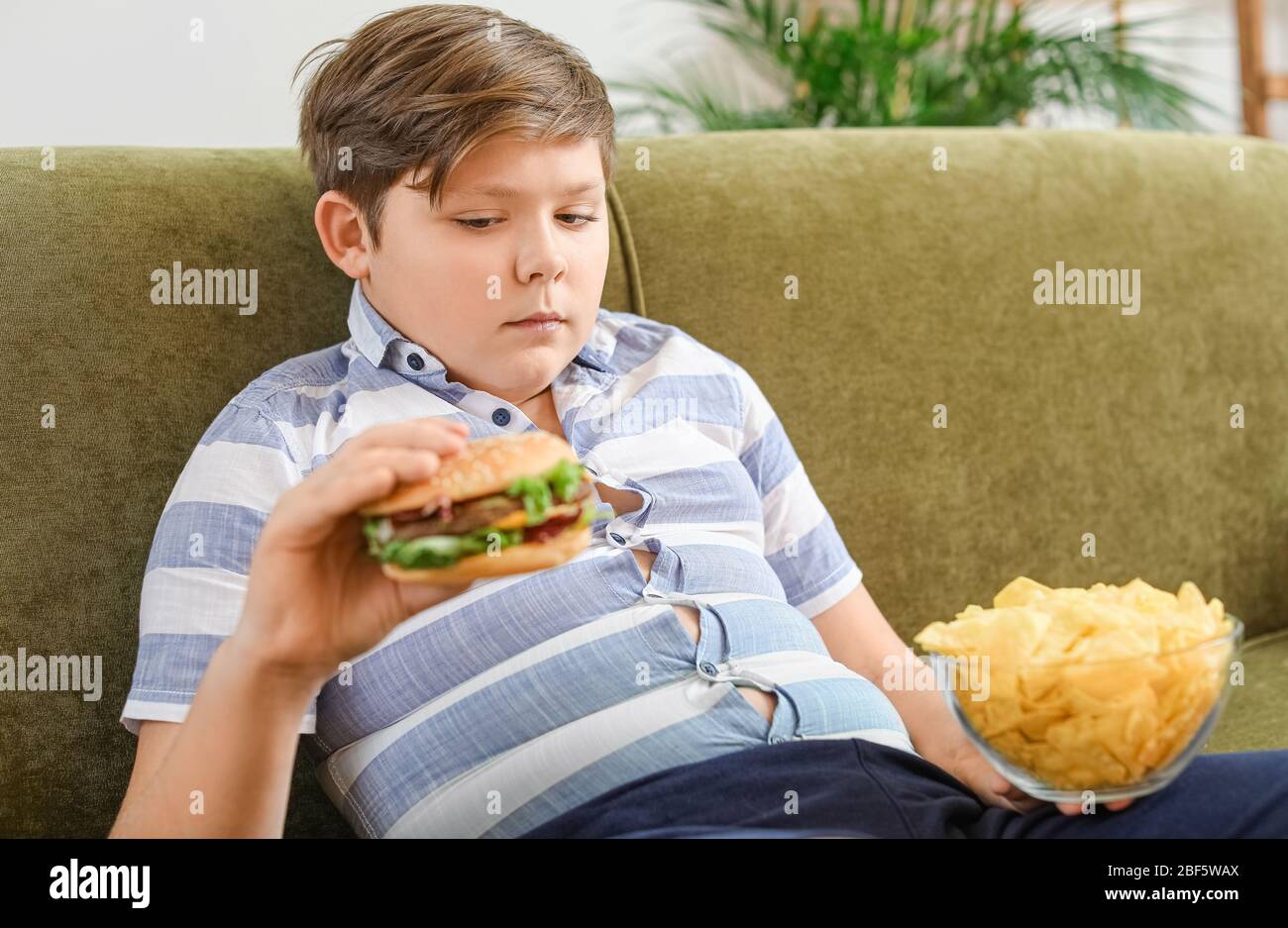 Overweight boy with junk food at home Stock Photo