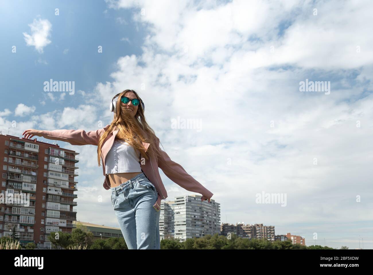 Young caucasian girl enjoys listening to music in a park in the city. Stock Photo