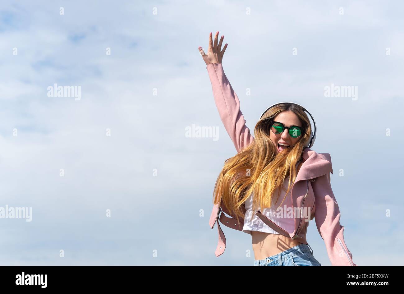 Young caucasian girl enjoys listening to music jumping for joy in a park in the city. Stock Photo
