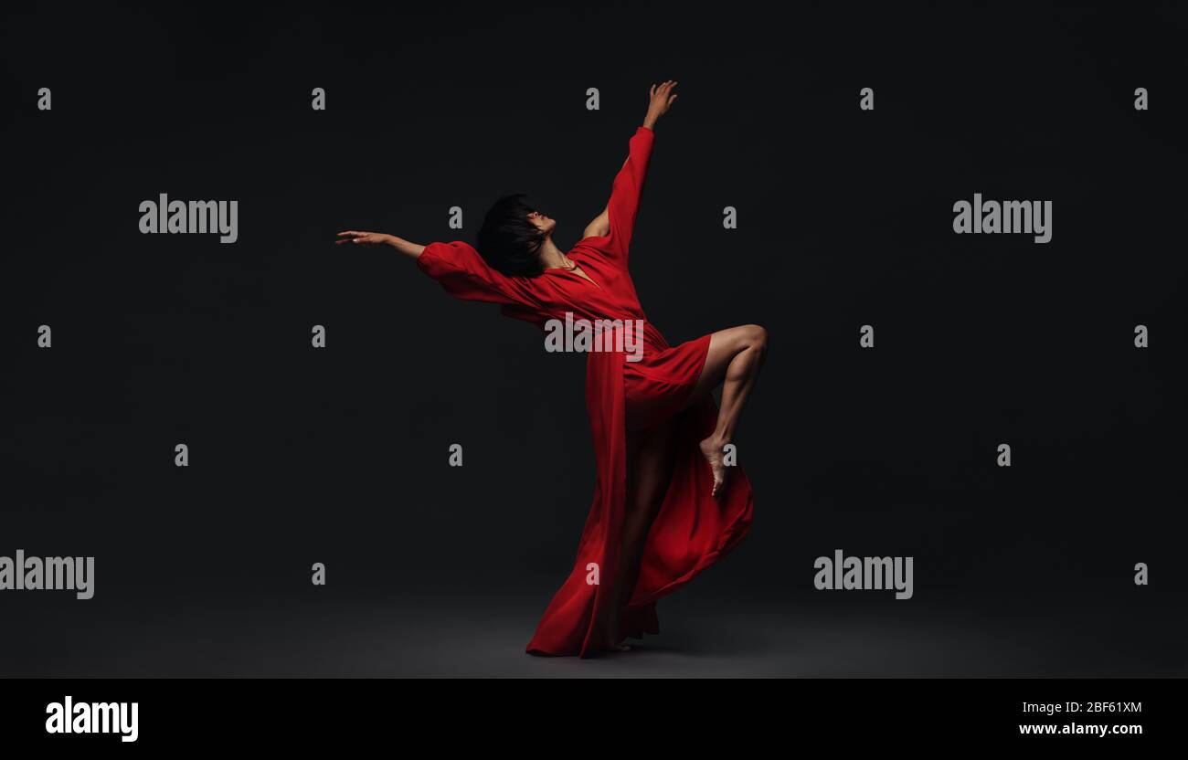 Female dancer performing contemporary dance style on black background. Woman in red dress dancing in studio. Stock Photo