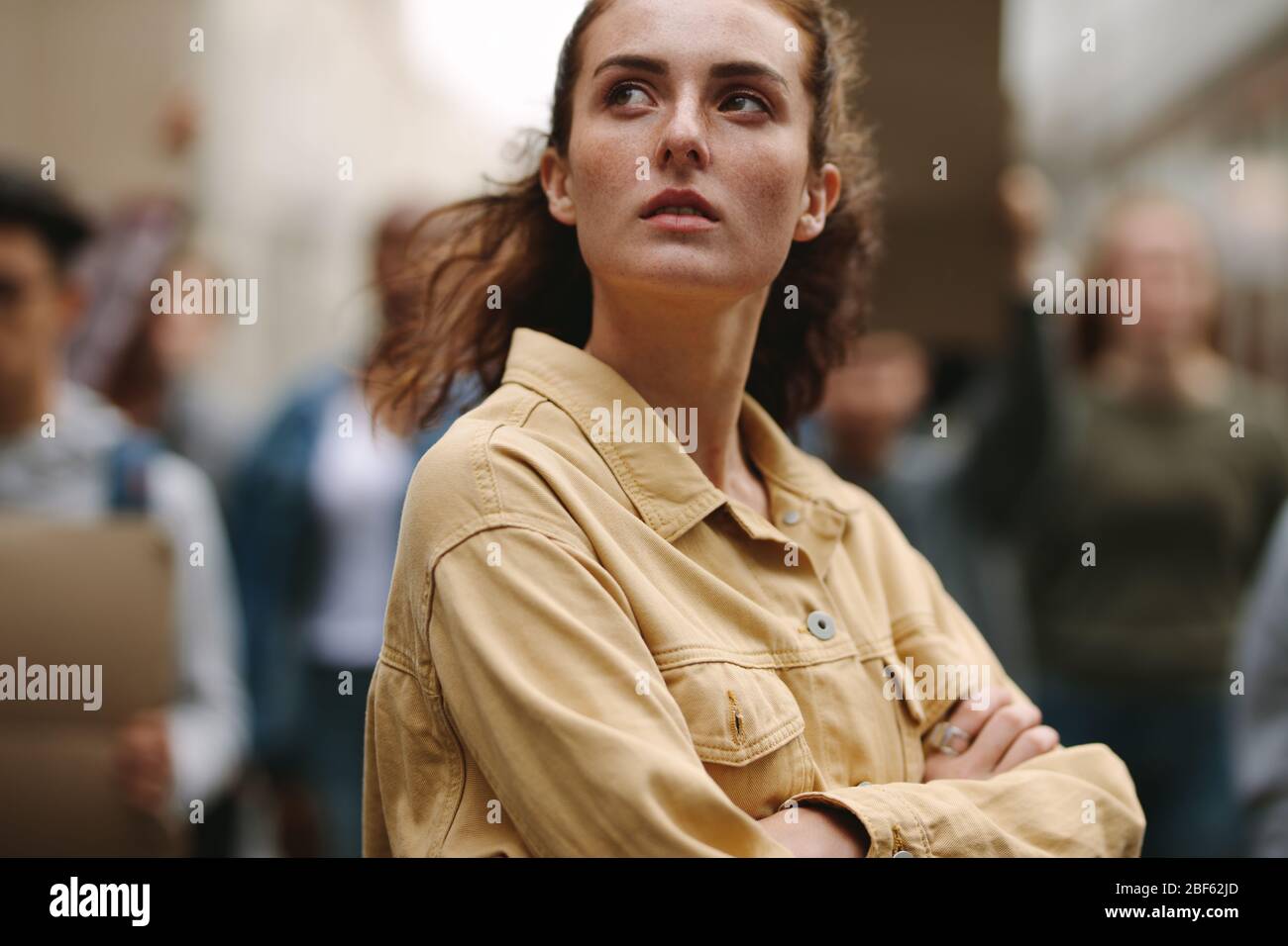 Young woman participate in a protest with demonstrator in background. Woman protesting with rebellions outdoors on road. Stock Photo