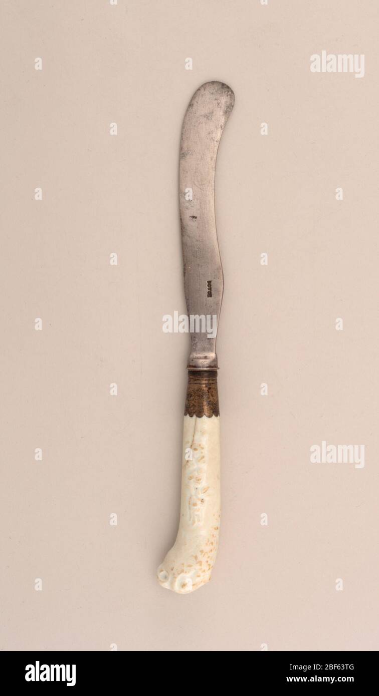 Knife. Sabre-shaped blade, plain bolster. silver ferrule with scalloped edge. Pistol-shaped white porcelain handle, decorated in relief with floral sprays and a parrot's head at the top of the handle. Stock Photo