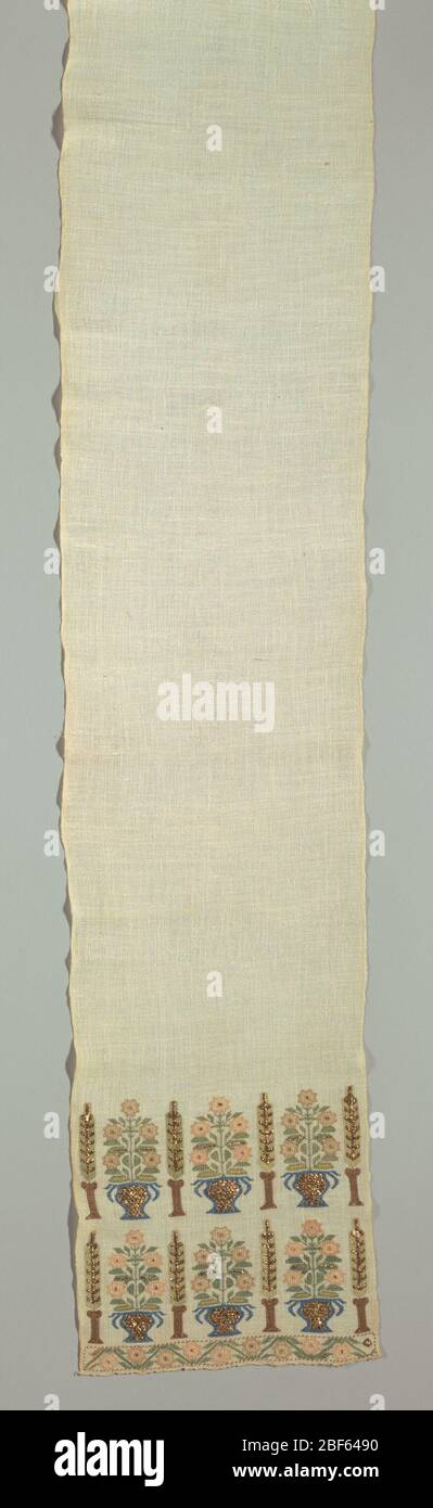 Towel. Towel of white hand-woven cotton, narrow width (9 1/16 in. from selvage to selvage). Ends embroidered in silk design of double row of stylized jars of flowers, alternating with tall trees. Colors: rose, green, and yellow and blue, flat gold. Stock Photo