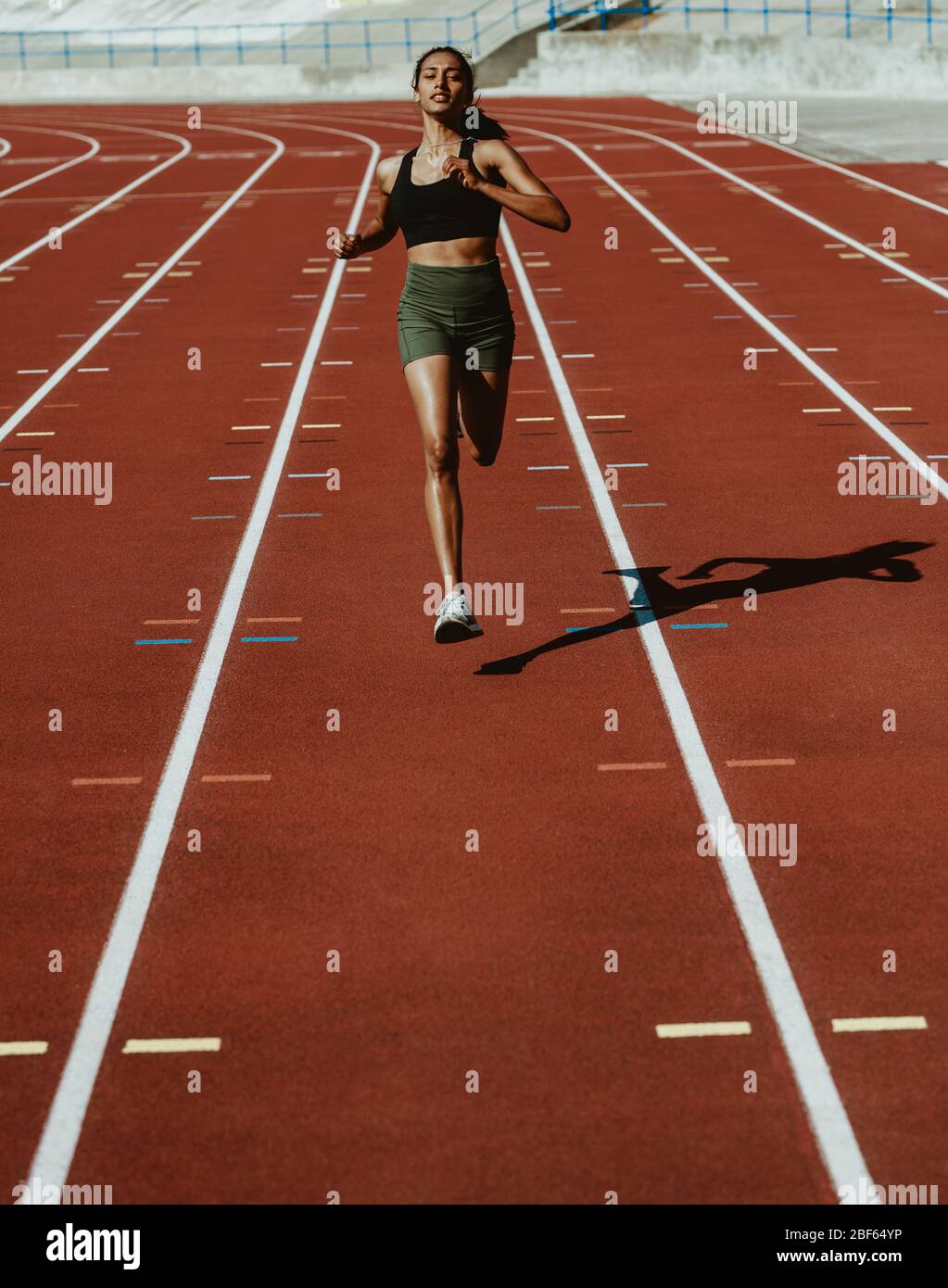 Female athlete sprinting on a running track in a track and field stadium. Woman runner training on a running track. Stock Photo