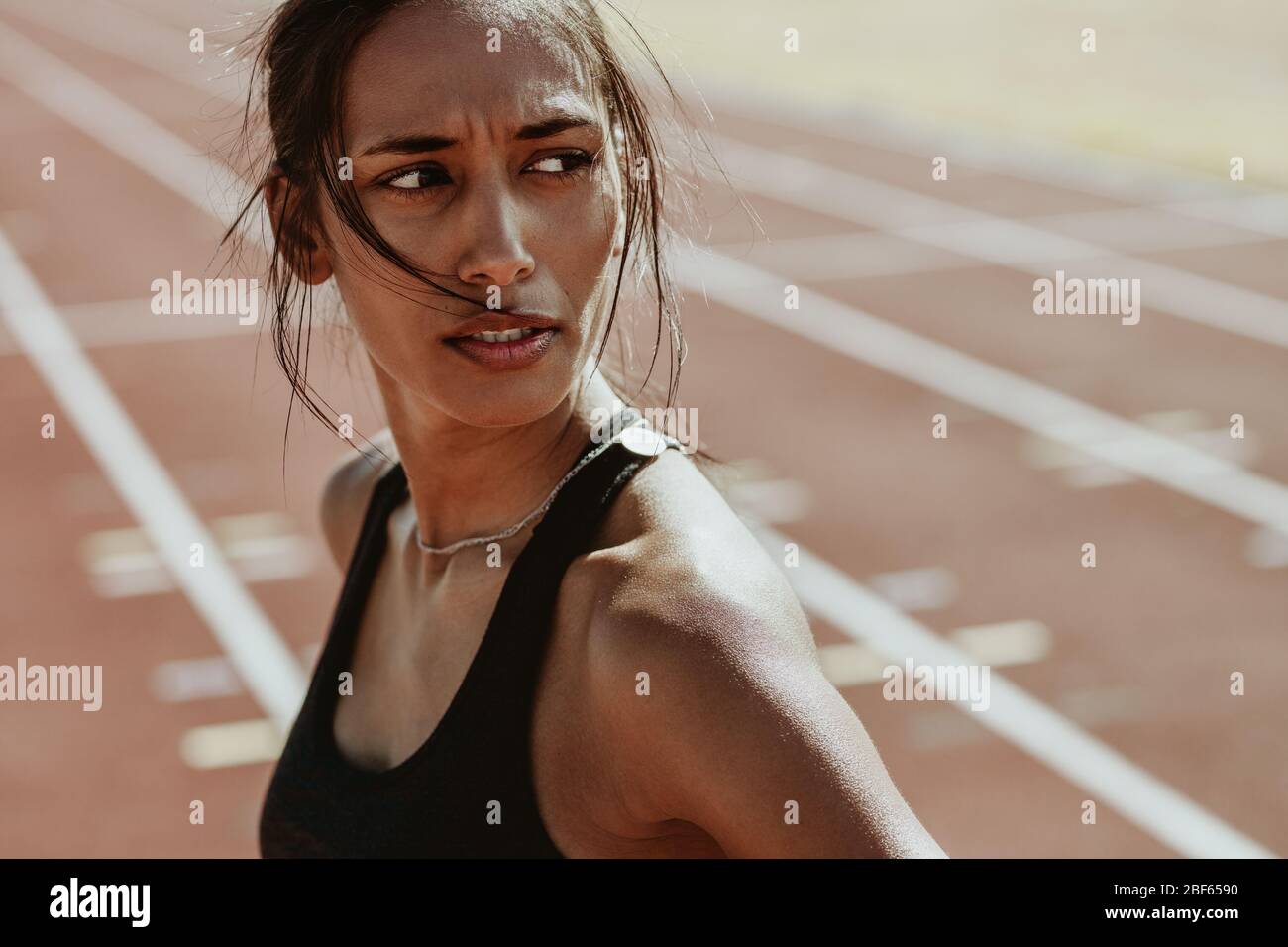 Close-up of a sportswoman after a run on the stadium track. Confident female athlete standing on track and looking away. Stock Photo