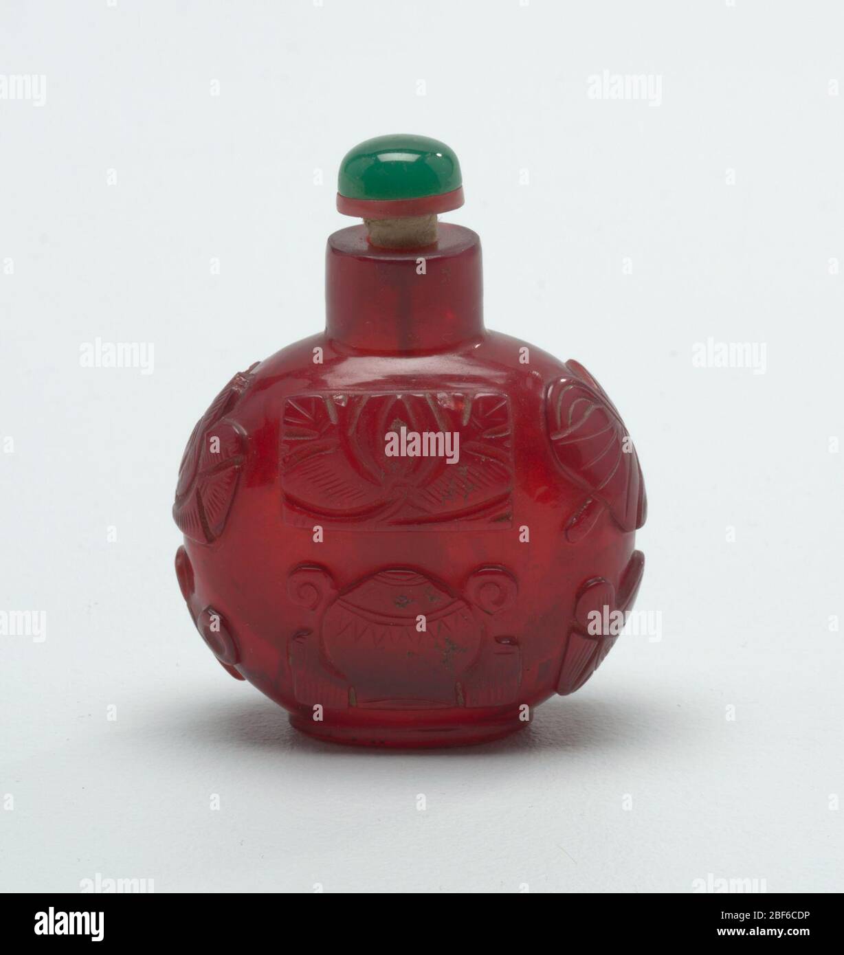 snuff bottle. Monotone cameo-glass, ruby red; carved with eight precious emblems of good fortune; wheel of law, conch shell, umbrella canopy, lotus flower, pair of fish, endless knot. Flattened globose shape. Stock Photo