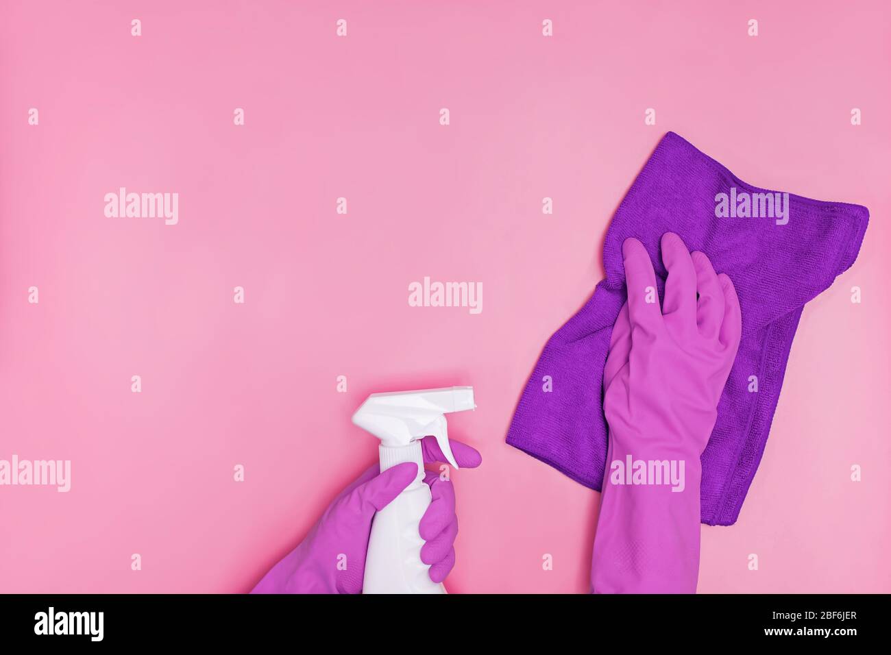 Hand in a rubber yellow glove holds pink bottle of liquid bleach on a