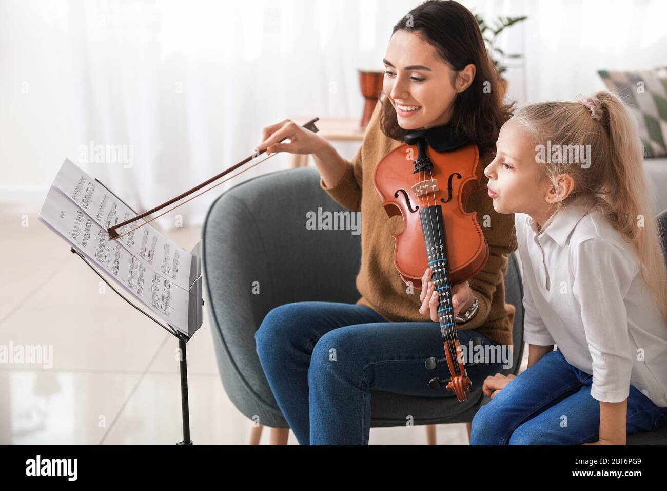 Private music teacher giving violin lessons to little girl at home ...